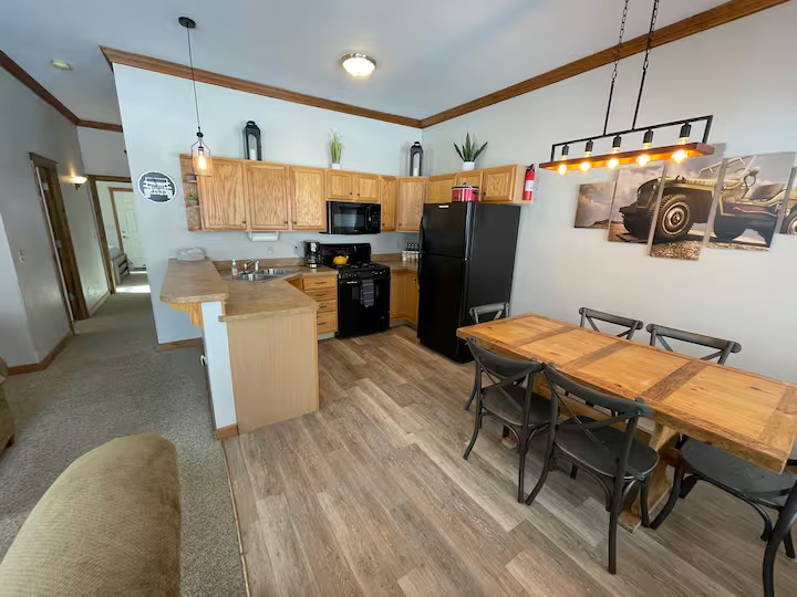 Kitchen with oak cabinets, a black refrigerator and range and a breakfast bar, with the dining table under pendant lights