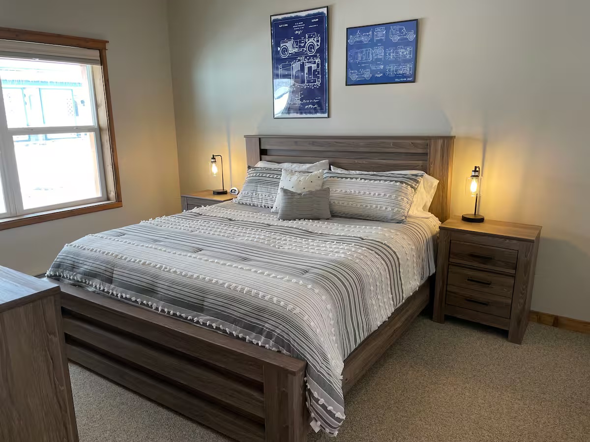 Bedroom with a wood headboard, bedside lamps and two framed Jeep patent drawings above the bed