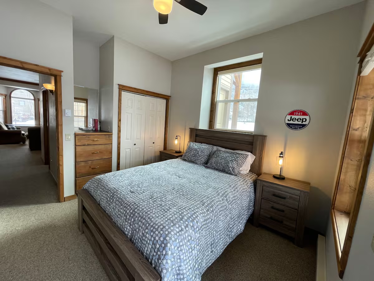 Bedroom with a closet, a tall dresser and a round vintage Jeep sign on the wall, looking through to the living room
