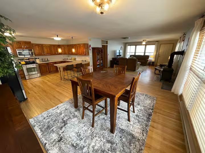 Dining table and chairs on a rug, with the open kitchen behind and the living room beyond