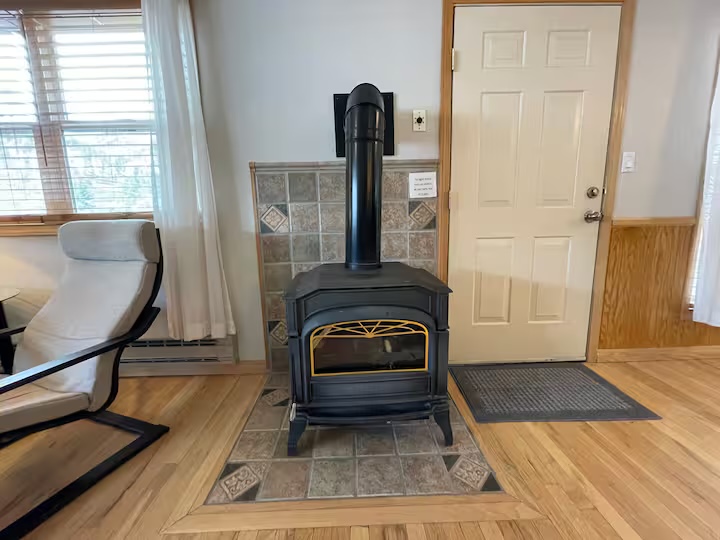 Gas stove on a tiled hearth beside the entry door, with a chair by the window