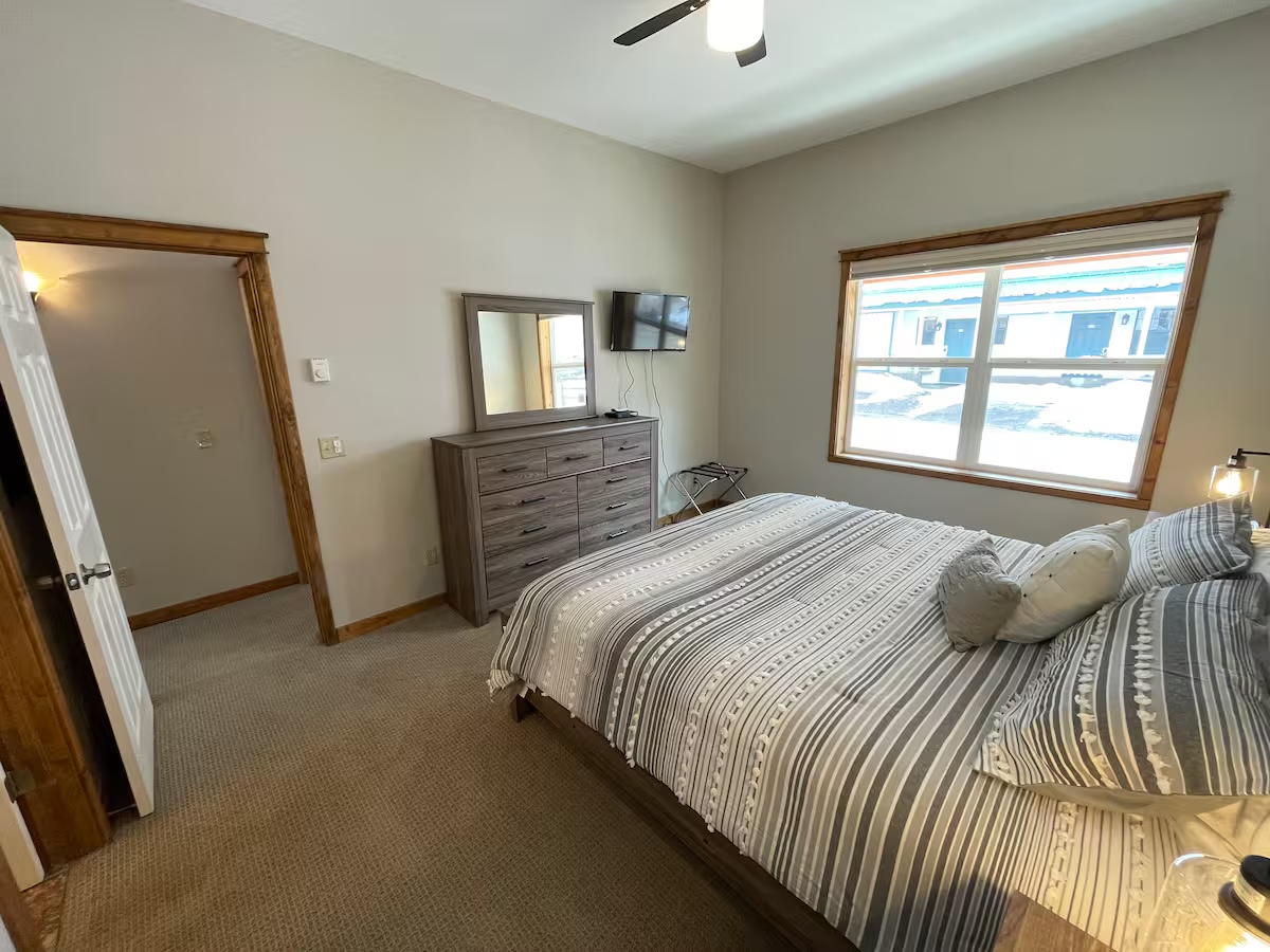 Bedroom with a dresser and mirror, a television and a luggage rack by the window