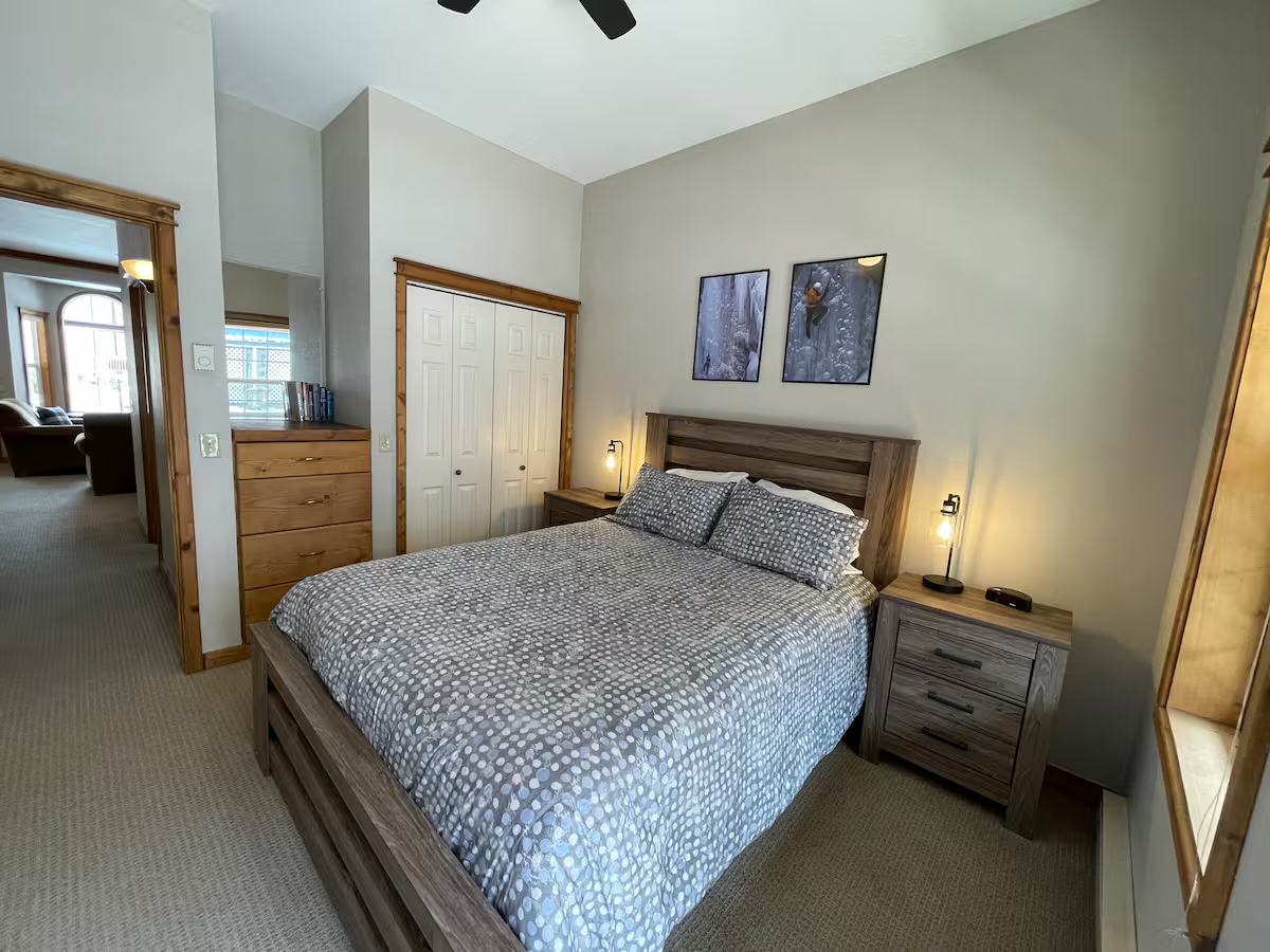 Bedroom with a closet, a dresser and two framed ice-climbing photographs above the bed, looking through to the living room