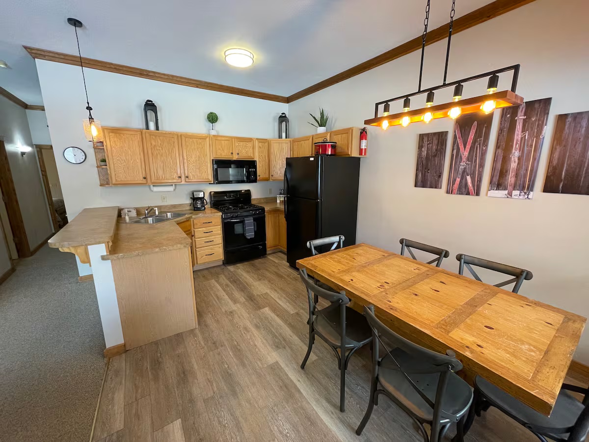 Kitchen with oak cabinets, a black refrigerator and gas range and a breakfast bar, with the dining table and ski canvases beyond