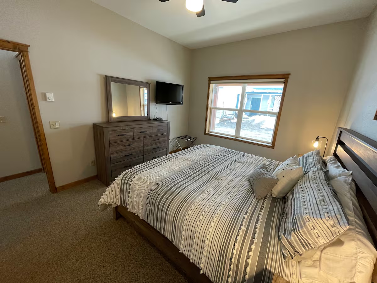 Bedroom with a dresser and mirror, a television and a luggage rack by the window