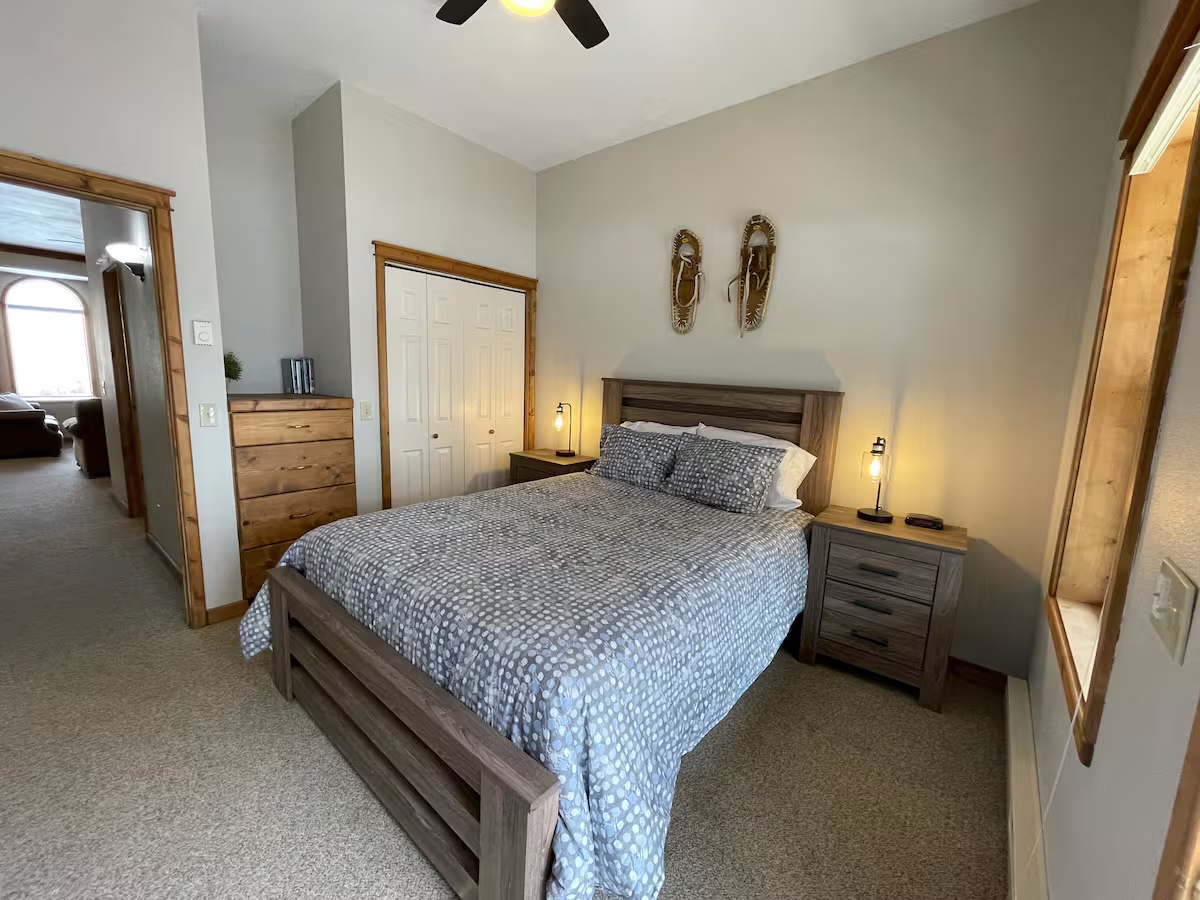 Bedroom with a closet, a pine dresser and snowshoes above the bed, looking through to the living room